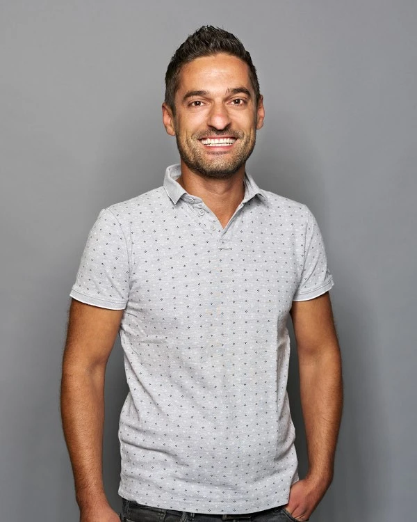 Rene Greiderer; -	Ein Mitarbeiter für Logistik und Disposition hat ein hellgraues Poloshirt mit Muster an, trägt seine kurzen Haare nach oben und hat einen Arm in der Hosentasche eingesteckt.